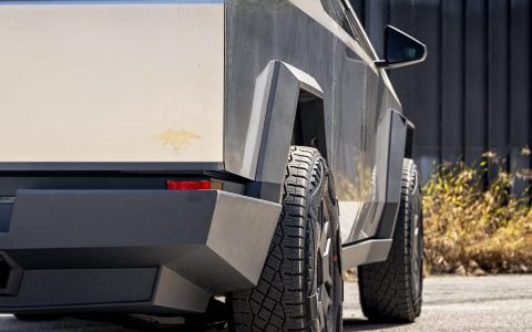Rear angle of Tesla Cybertruck displaying the effect of 50mm wheel spacers by Unplugged Performance. The widened track and rugged tire fitment highlight the Cybertruck's bold design and off-road readiness, set against an industrial backdrop.