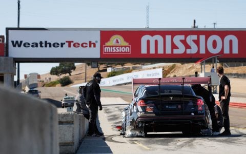 Tesla Model S Plaid 'Dark Helmet' in the pit lane at Laguna Seca during the GridLife event. The car features Unplugged Performance aerodynamic upgrades and Casa Bonita branding on the rear wing. Team members stand nearby, monitoring performance and making adjustments before the next session.