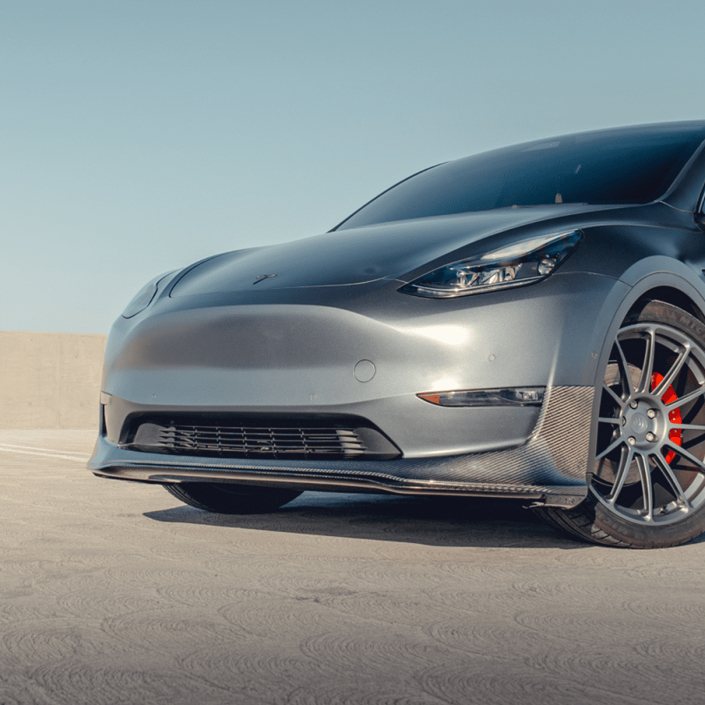 Unplugged Performance Tesla Model Y with 21-inch UP-03 wheels, lowered stance, featuring a carbon fiber diffuser and spoiler, parked on a rooftop with a clear blue sky background.